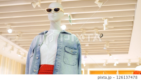 Stylish mannequin displays current fashion trends, showcasing a denim jacket, white shirt, and a vibrant red skirt in a brightly lit retail environment. Concept fashion clothes 126137478