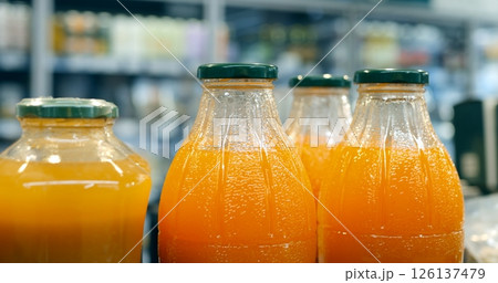 Multiple glass bottles filled with orange juice are neatly arranged on a supermarket shelf, creating a vibrant display against a backdrop of other products Multiple glass bottles filled with orange juice are neatly arranged on a supermarket shelf, creating a vibrant display against a backdrop of other products 126137479