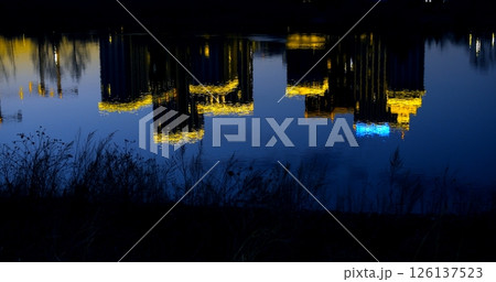 Urban skyline mirroring on a tranquil body of water at night, creating a captivating symmetrical view of illuminated buildings and their reflections 126137523