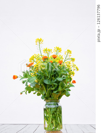 Yellow and orange flowers in glass bowl stand on table against white wall 126137796