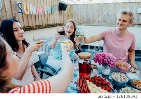 Friends toasting cocktails, enjoying summer gathering on private outdoor patio terrace with drinks and snacks. Friends dining, having fun together on patio party event. Selective focus 126138043
