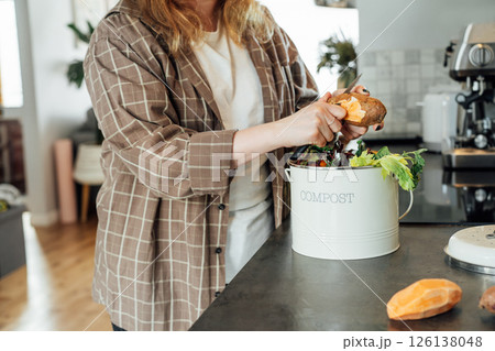 Compost the kitchen waste, recycling at home. Woman putting vegetables cutted leftovers into the garbage, compost bin on the table of kitchen. Environmentally responsible, ecology. Selective focus 126138048