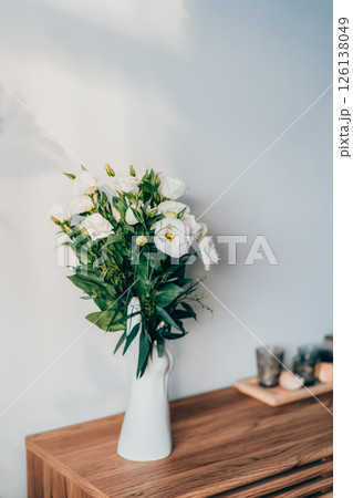 Fresh eustoma flowers bouquet in stylish white ceramic vase made in the shape of human hand on the wooden console. Trendy interior design decor details. Vertical card. Selective focus. 126138049