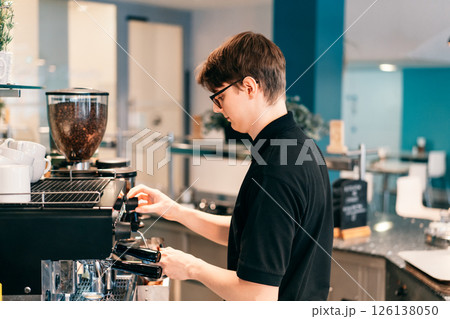 Young barista making coffee at automatic machine in a modern coffee shop. Student working part-time in cafe. Problems of unemployment and Job opportunities for youth. Small business vacancies 126138050