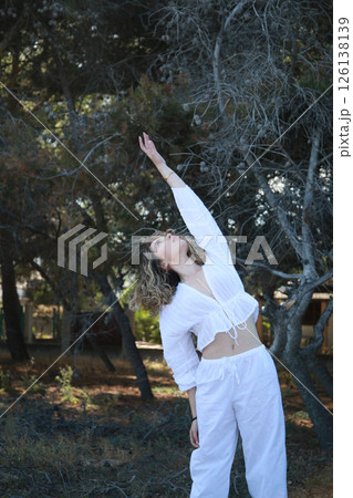 Young White Dressed Woman Warms Her Arms Near The Pine Forest In The Mountains Young White Dressed Woman Warms Her Arms Near The Pine Forest In The Mountains 126138139