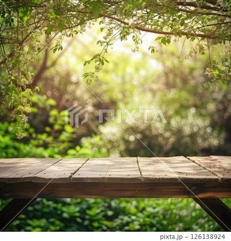 An inviting spring background filled with vibrant green leaves, blooming flowers, and an empty wooden table illuminated by sunlight. 126138924