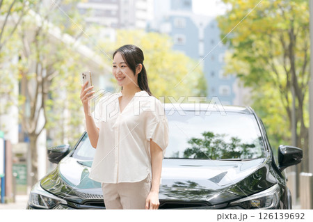 車の前でスマホを操作する若い女性 126139692