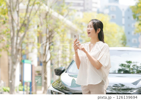 車の前でスマホを操作する若い女性 126139694