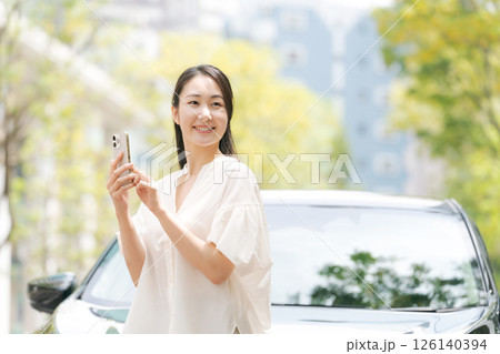 車の前でスマホを見る女性 126140394