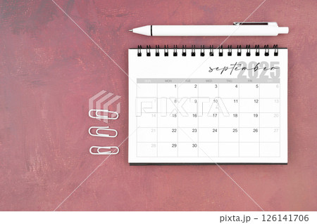 Desk calendar for September 2025 and pen with paper clips on red table. Desk calendar for September 2025 and pen with paper clips on red table. 126141706