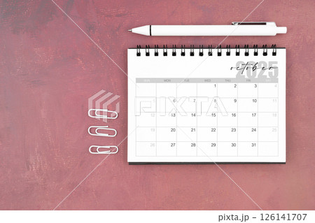 Desk calendar for October 2025 and pen with paper clips on red table. Desk calendar for October 2025 and pen with paper clips on red table. 126141707