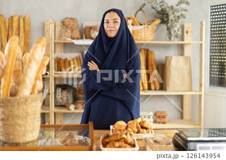 Muslim girl seller employee puts croissants in window, arranges display of goods at bakery. 126143954