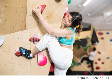Young Asian woman climbs steep artificial wall in sports complex and trains endurance 126144051