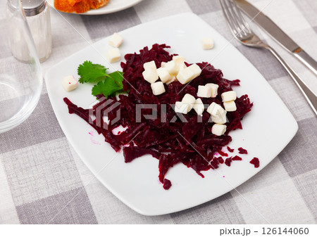 On plate is portion of salad of grated boiled beetroot with addition of small pieces of white cheese. On plate is portion of salad of grated boiled beetroot with addition of small pieces of white cheese. 126144060
