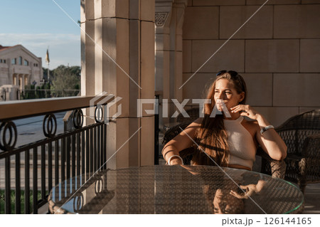 Woman Balcony View Relaxation - A woman sits on a balcony, enjoying a view of the city in the afternoon. 126144165