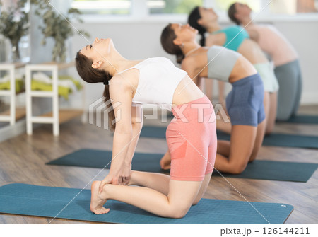 Young girl teaches yoga lesson, shows students technique of performing camel pose, Ushtrasana asana Young girl teaches yoga lesson, shows students technique of performing camel pose, Ushtrasana asana 126144211