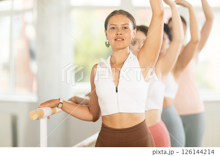 Group ballet rehearsal - young ballerinas stand in third position near ballet barre during group training in dance studio 126144214