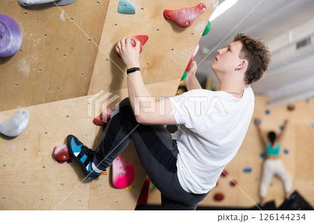 Teenage boy climbs steep artificial wall in sports complex and trains endurance Teenage boy climbs steep artificial wall in sports complex and trains endurance 126144234