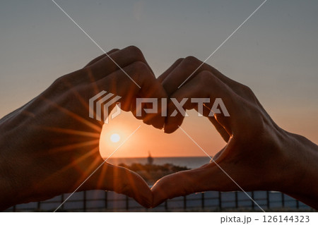 Sunset Heart Hands Beach - Silhouette of hands framing a sunset over the beach, forming a heart shape. 126144323