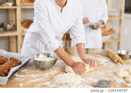Cute doughs arranged on table in bakery with close-up of woman's hands skillfully kneading dough at food production line Cute doughs arranged on table in bakery with close-up of woman's hands skillfully kneading dough at food production line 126144597