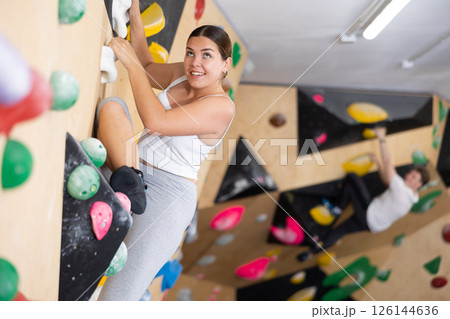 Young Europian woman climbs steep artificial wall in sports complex and trains endurance Young Europian woman climbs steep artificial wall in sports complex and trains endurance 126144636