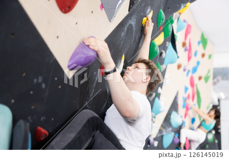 Teen guy practicing rock climbing on climbing wall 126145019