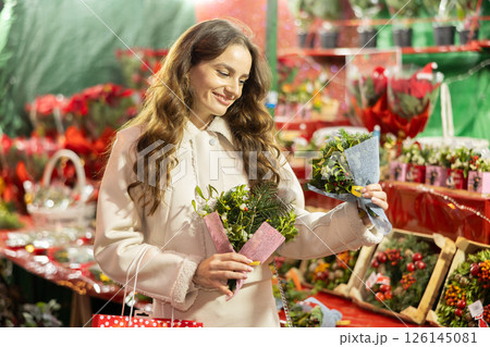 Smiling woman choosing festive home decorations on street Christmas fair Smiling woman choosing festive home decorations on street Christmas fair 126145081