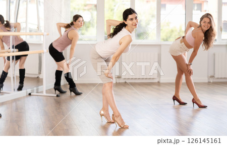 Graceful women blending sensuality with fashion while partaking in group high heels dance class Graceful women blending sensuality with fashion while partaking in group high heels dance class 126145161
