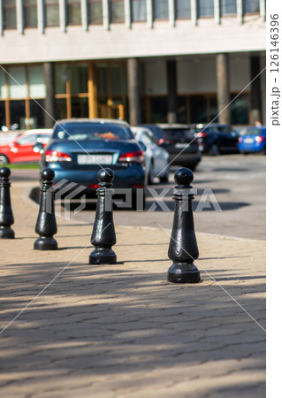 A long row of black poles standing on a sidewalk, with cars in the background 126146396