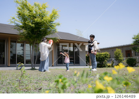 平屋の戸建ての庭の前でボールを投げて遊ぶ家族と子供の幸せの不動産のファミリーイメージ　緑の前ボケ 126146489