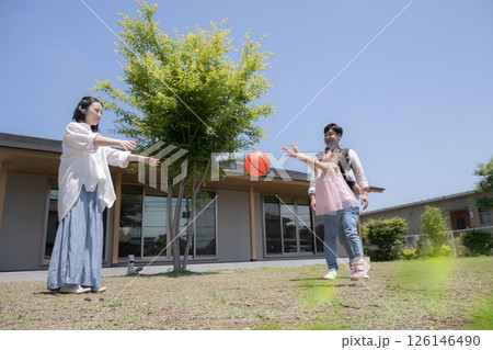 平屋の戸建ての庭の前でボールを投げて遊ぶ家族と子供の幸せの不動産のファミリーイメージ　緑の前ボケ 126146490