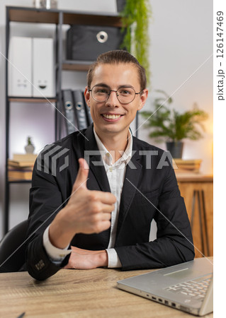 Smiling young Caucasian businessman freelancer showing double thumbs up sitting at home office desk Smiling young Caucasian businessman freelancer showing double thumbs up sitting at home office desk 126147469