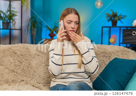 Caucasian woman sad call holding mobile phone shocked face emotional empathy sorrow on sofa at home Caucasian woman sad call holding mobile phone shocked face emotional empathy sorrow on sofa at home 126147479