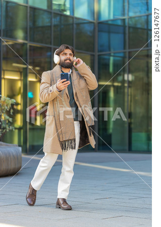 Happy young man putting on headphones listening favorite energetic music on smartphone on street 126147677