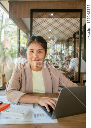 A young woman in a cafe working on her laptop, surrounded by modern decor and natural light. A young woman in a cafe working on her laptop, surrounded by modern decor and natural light. 126148328