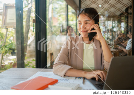 Professional woman multitasking with phone and laptop in a bright, modern office setting, showcasing productivity and communication. Professional woman multitasking with phone and laptop in a bright, modern office setting, showcasing productivity and communication. 126148330