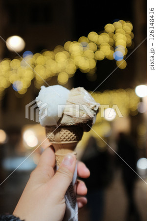 Italian gelato close up in hand and shop scene at Rome night market with decorative lights and festive crowd. High quality photo 126148416