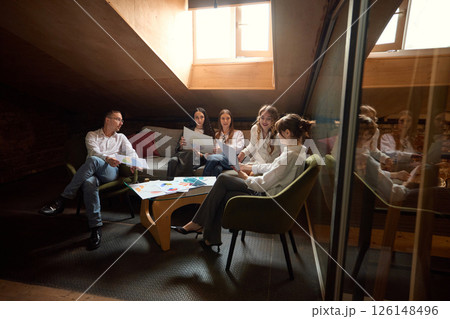 Business team reviews documents in office lounge area, sitting on sofa and chairs, discussing strategy. Business team reviews documents in office lounge area, sitting on sofa and chairs, discussing strategy. 126148496