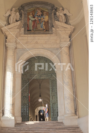 Swiss Guard in traditional Renaissance uniform holding ceremonial halberd under arched marble doorway inside Vatican City with dramatic light and historic architecture guarding entrance to sacred area Swiss Guard in traditional Renaissance uniform holding ceremonial halberd under arched marble doorway inside Vatican City with dramatic light and historic architecture guarding entrance to sacred area 126148663