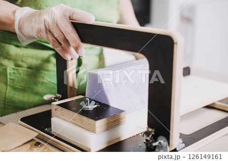 Close-up of a woman slicing handmade purple soap bars using a wire soap cutter. Small-batch skincare, craftpreneur economy, home-based entrepreneurship, creative business models Close-up of a woman slicing handmade purple soap bars using a wire soap cutter. Small-batch skincare, craftpreneur economy, home-based entrepreneurship, creative business models 126149161