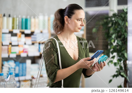 Woman scans mobile barcode of cosmetics in pharmacy 126149614