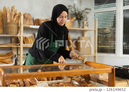 Saleswoman in a hijab collects pastries in a container 126149652