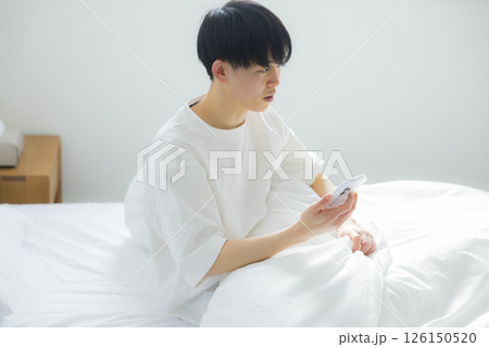 ベッドでスマートフォンを使う男性　 126150520