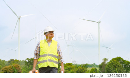 Engineer walking through wind farm with toolbox and blueprint for renewable energy maintenance and inspection 126150586