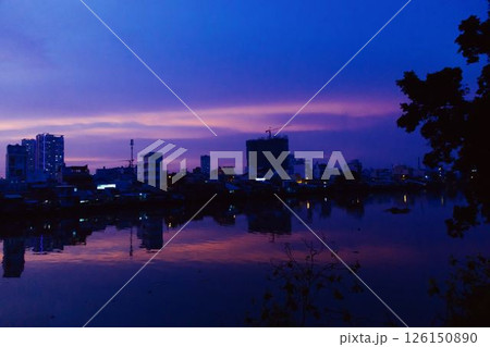 Stunning pink and purple sunset sky reflecting on calm river with silhouetted city skyline and peaceful twilight atmosphere in urban landscape at dusk. High quality photo Stunning pink and purple sunset sky reflecting on calm river with silhouetted city skyline and peaceful twilight atmosphere in urban landscape at dusk. High quality photo 126150890