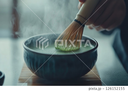Hand whisking matcha tea in a traditional bowl with steam rising in a serene setting Hand whisking matcha tea in a traditional bowl with steam rising in a serene setting 126152155