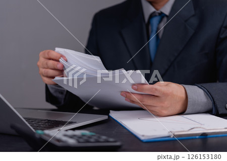 Businessman reviewing financial documents and reports. Office paperwork, data analysis, corporate management, financial review, business planning, and accounting operations. Businessman reviewing financial documents and reports. Office paperwork, data analysis, corporate management, financial review, business planning, and accounting operations. 126153180