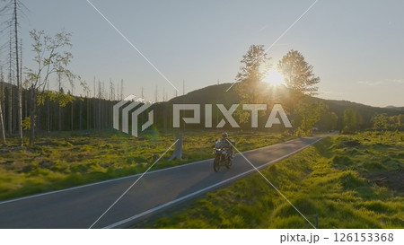 Driver riding motorcycle on empty asphalt road, spring mountains during sunset Driver riding motorcycle on empty asphalt road, spring mountains during sunset 126153368