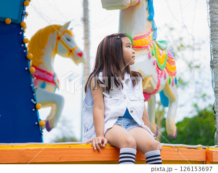 Asian girl having fun in amusement park, enjoying carousel on family vacation. 126153697