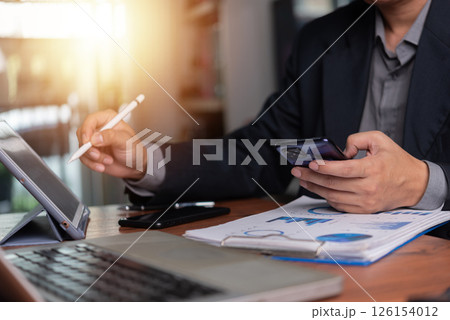 Business executive using a tablet and smartphone to analyze financial data for corporate strategy. 126154012
